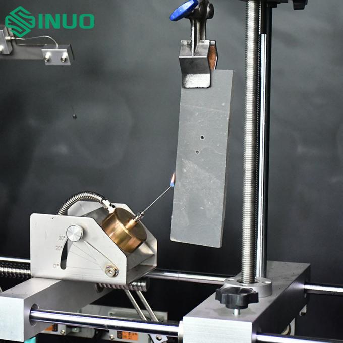 Needle flame test apparatus SN773 showing the Φ0.9mm stainless steel needle burner tilted at 45 degrees inside the stainless steel test chamber with black background